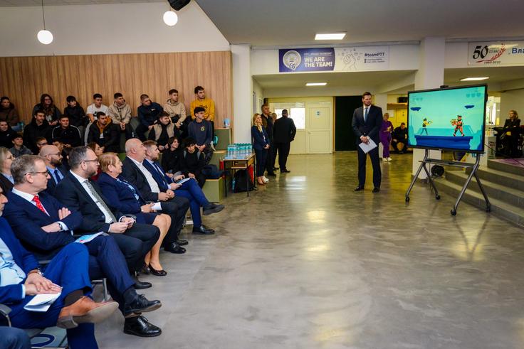 Audience watches presenter with a screen in a conference room.