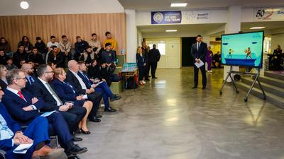 Audience watches presenter with a screen in a conference room.